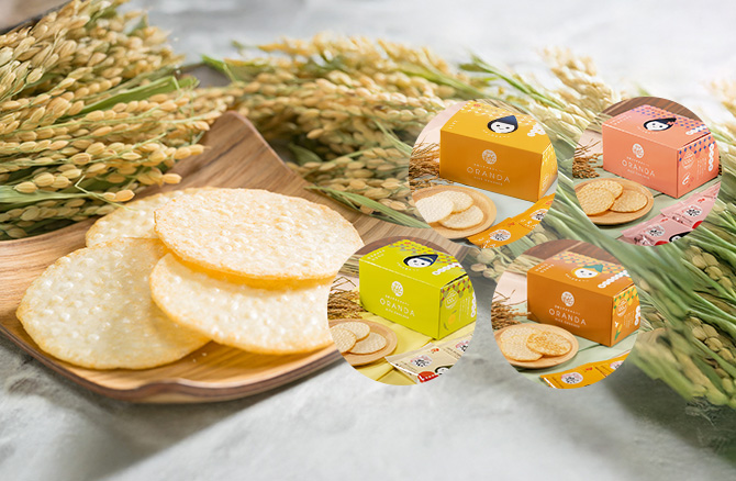 稲穂を背景に、色違いの4つのギフト箱と丸いオランダせんべいが並ぶ写真。